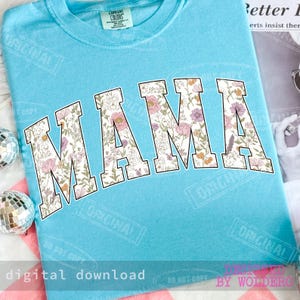 May include: A light blue t-shirt with the word "MAMA" in large, floral-patterned letters. The floral design includes pink, purple, and yellow flowers. The shirt has a crew neck and the text "digital download" is at the bottom.
