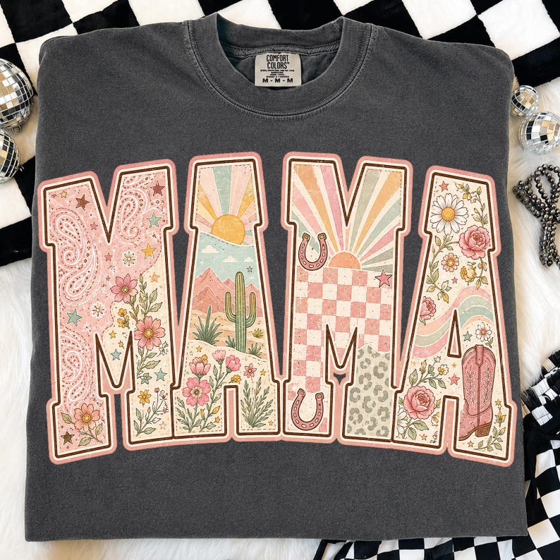 Puede incluir: Una sudadera de cuello redondo gris carb&oacute;n con la palabra MAMA en letras grandes. Cada letra contiene un dise&ntilde;o gr&aacute;fico &uacute;nico que incluye paisajes des&eacute;rticos, cactus, soles, herraduras, patrones de cuadros, flores y una bota vaquera.