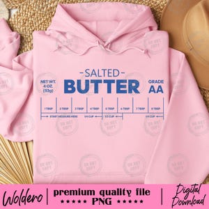 Könnte beinhalten: Ein hellrosa Kapuzenpullover mit einem grafischen Design zum Abmessen von Butter. Das Design enthält die blauen Wörter "SALTED BUTTER", Messmarkierungen und den Text "NET WT. 4 OZ. (113g)". Der Hoodie hat auch den Text "premium quality file PNG" und "Digital Download".