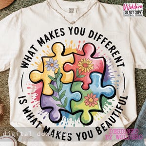 以下が含まれることがあります： クリーム色のTシャツ。カラフルなパズルデザインと「WHAT MAKES YOU DIFFERENT IS WHAT MAKES YOU BEAUTIFUL」の文字がプリントされています。パズルのピースには花の装飾が施されています。このシャツはクルーネックで半袖です。