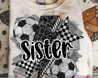 May include: A beige sweatshirt featuring a graphic design with the word "SISTER" in bold white letters. The design includes soccer balls, lightning bolts with leopard print, and checkered stars. The words "digital download" and "designed by wonder" are also visible.