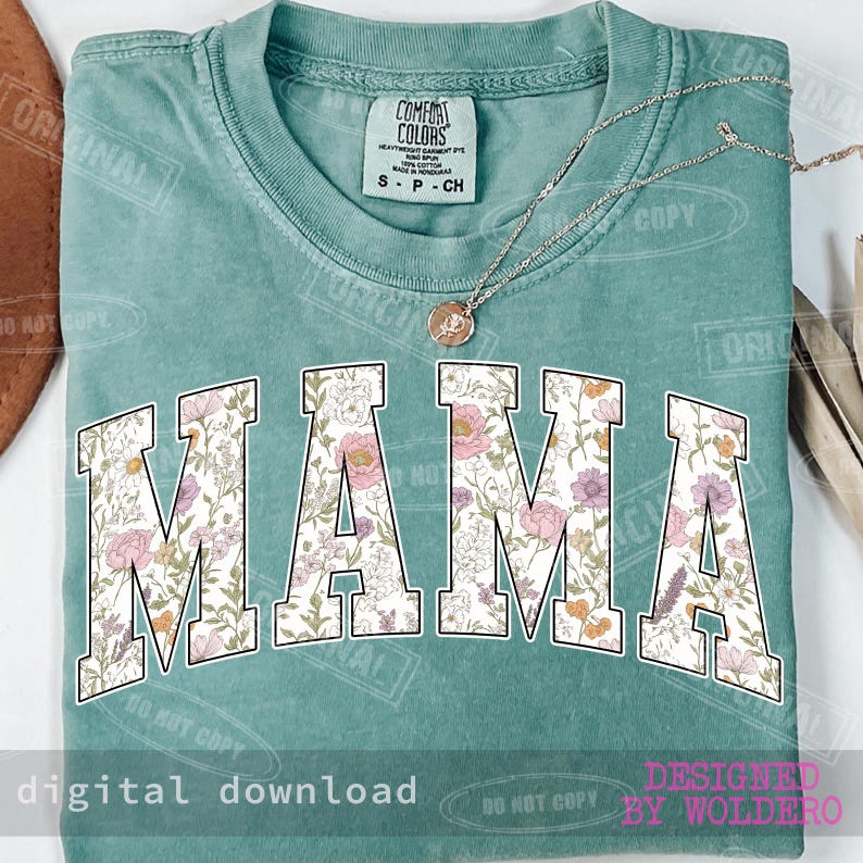 May include: A teal Comfort Colors t-shirt with the word "MAMA" in large, floral-patterned letters across the front. A delicate necklace with a pendant rests on the shirt. The words "digital download" and "designed by woldero" are also visible.