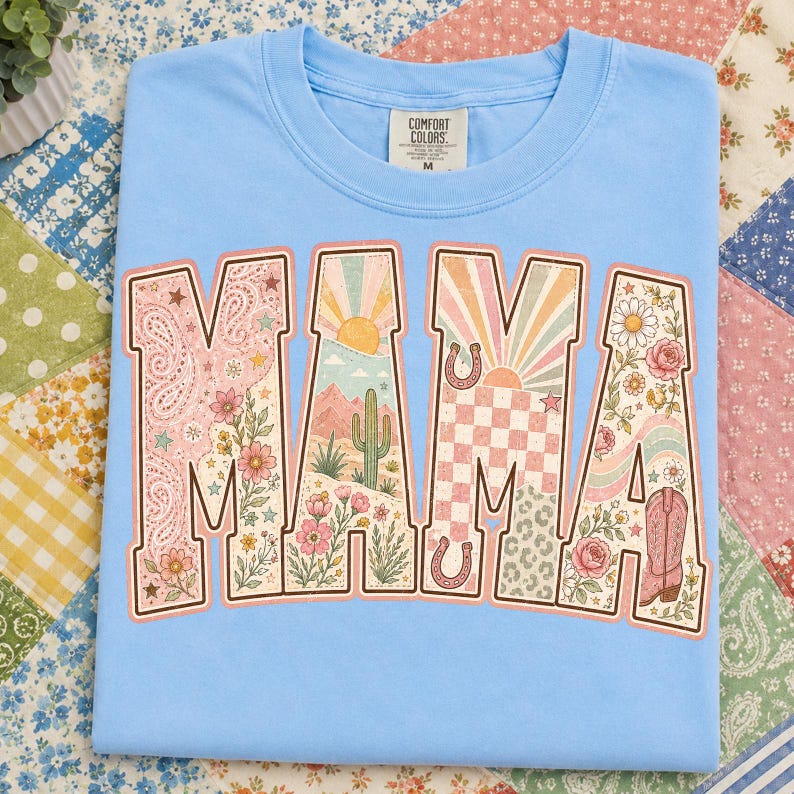 Puede incluir: Una camiseta azul claro con una etiqueta Comfort Colors en el cuello. El frente presenta la palabra MAMA en letras grandes, cada una rellena con un patr&oacute;n diferente que incluye cachemir, paisajes des&eacute;rticos con cactus, soles, cuadros y motivos florales.