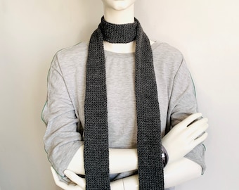 May include: A gray knitted scarf on a white mannequin. The scarf is long and thin, and it is folded in half.