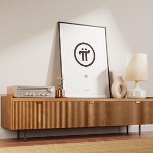 May include: A black framed poster with a white background and a black circle containing the symbol "π" and the word "Pi" underneath. The poster is hanging on a wall above a wooden cabinet with two doors. A lamp with a white shade and a ceramic base is on the cabinet, along with a small vase with dried flowers and a ceramic sculpture.