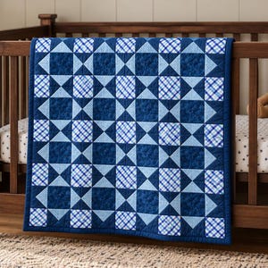 May include: A patchwork quilt featuring a repeating geometric pattern of dark blue solid squares, light blue solid squares, and white squares with a blue plaid design. The quilt is draped over the side of a wooden crib with a dark brown finish.