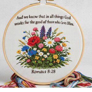 May include: A cross-stitch embroidery hoop featuring a floral bouquet with red poppies, blue cornflowers, and white daisies. The text reads, "And we know that in all things God works for the good of those who love Him. Romans 8:28."