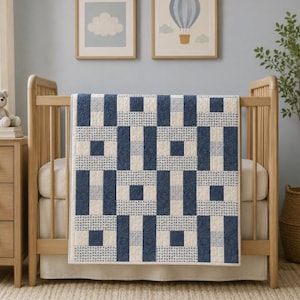 Puede incluir: Una colcha rectangular con un patrón geométrico de cuadrados azul marino sólidos, rectángulos color crema sólidos y cuadrados azul claro con un patrón de pequeños puntos blancos, dispuestos en una cuadrícula estructurada.