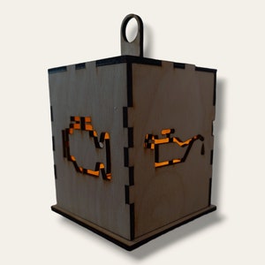 Może przedstawiać: Drewniana skrzynka z wyciętym symbolem kontrolki silnika i symbolem kanistra oleju. Skrzynka jest podświetlona od wewnątrz, tworząc ciepłe światło.