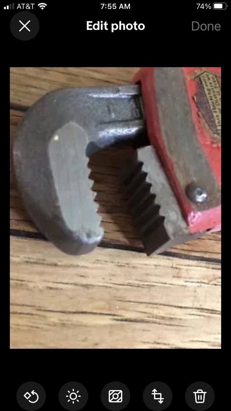 May include: Close-up of a red and silver adjustable wrench with a serrated jaw. The wrench is resting on a wooden surface.