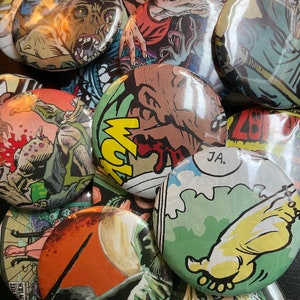 Könnte beinhalten: Eine Sammlung runder, bunter Knöpfe mit Comic-Illustrationen. Die Knöpfe zeigen verschiedene Szenen mit Monstern, Kreaturen und Figuren. Einige Knöpfe haben Text, darunter "JA."
