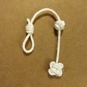 Könnte beinhalten: Ein weißes Seil mit zwei Knoten an den Enden. Die Knoten haben die Form einer Blume.