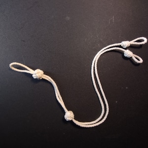 May include: A white cord with four knots tied in it. The cord is looped and forms an 'S' shape.