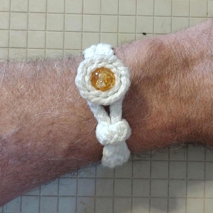 May include: A white ceramic mug with a black handle and the text "But First, Coffee" in a bold, black font. The mug is set against a blurred background, suggesting a cozy setting.