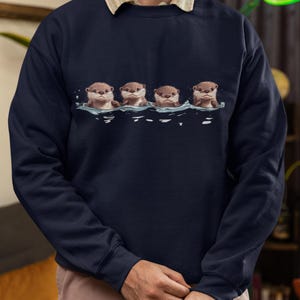 This unisex heavy blend crewneck sweatshirt shows cute otter offspring floating in a row. The adorable otter puppies are looking right at you, creating a whimsical and playful vibe. Perfect for animal lovers and those who enjoy cute, quirky designs.