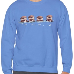 Op de afbeelding: Een blauw sweatshirt met een afbeelding van vier otters die in een rij zwemmen. De otters zijn bruin en hebben witte buiken. De afbeelding is gecentreerd op het sweatshirt.