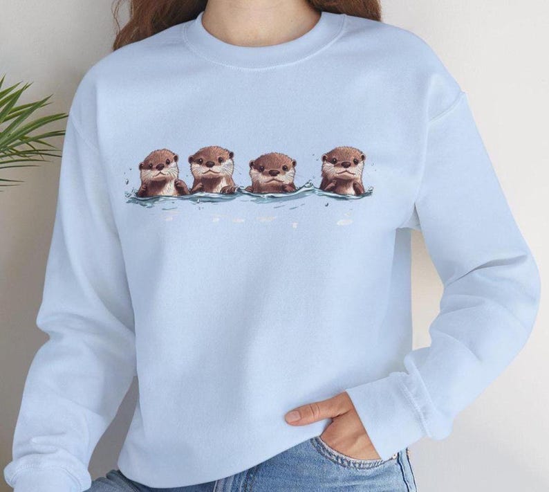 This unisex heavy blend crewneck sweatshirt shows cute otter offspring floating in a row. The adorable otter puppies are looking right at you, creating a whimsical and playful vibe. Perfect for animal lovers and those who enjoy cute, quirky designs.