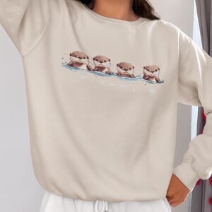 This unisex heavy blend crewneck sweatshirt shows cute otter offspring floating in a row. The adorable otter puppies are looking right at you, creating a whimsical and playful vibe. Perfect for animal lovers and those who enjoy cute, quirky designs.