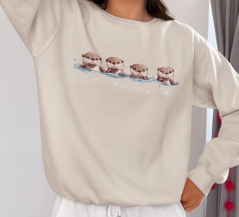 This unisex heavy blend crewneck sweatshirt shows cute otter offspring floating in a row. The adorable otter puppies are looking right at you, creating a whimsical and playful vibe. Perfect for animal lovers and those who enjoy cute, quirky designs.