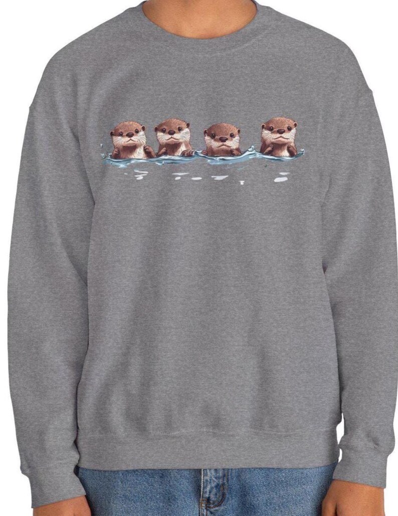 Op de afbeelding: Een grijs sweatshirt met een afbeelding van vier otters die in een rij zwemmen. De otters zijn bruin en hebben schattige gezichten.