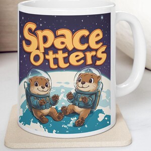 May include: White ceramic mug featuring the words "Space Otters" in orange lettering. The mug showcases two cartoon otters in space suits against a backdrop of a planet and starry sky. The otters are brown with blue space suits.