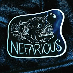 May include: Black and white sticker with a drawing of a anglerfish with the word "NEFARIOUS" written below it.
