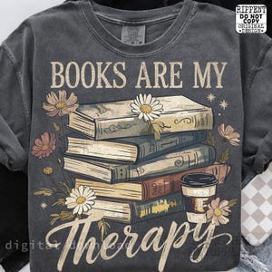 May include: Dark gray sweatshirt with the text "BOOKS ARE MY Therapy" in a whimsical font. The design features a stack of books, flowers, and a coffee cup. The graphic is in shades of beige, brown, and pink.