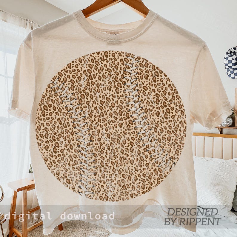 May include: Cream-colored t-shirt featuring a large baseball design with a leopard print pattern. The baseball design has white stitching details. The words "digital download" and "DESIGNED BY RIPPENT" are printed at the bottom of the shirt.