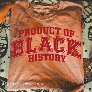 May include: A peach-colored t-shirt with the words "PRODUCT OF BLACK HISTORY" in red, collegiate-style lettering. The shirt is folded and held by hands. The words "digital download" and "DESIGNED BY RIPPENT" are also visible.