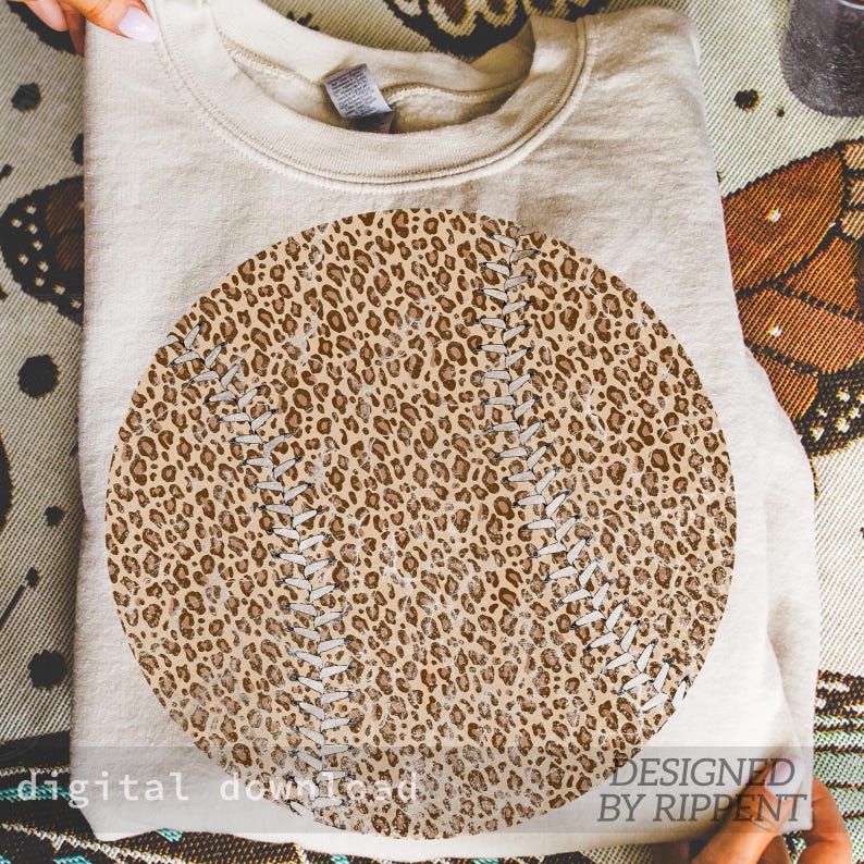 May include: A beige sweatshirt with a large baseball design. The baseball graphic features a leopard print pattern with white stitching details. The words "digital download" and "designed by Rippent" are printed on the bottom of the image.
