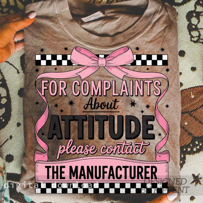 May include: A brown t-shirt with a pink bow and the text "FOR COMPLAINTS About ATTITUDE please contact THE MANUFACTURER". The design includes black and white checkered patterns and pink ribbons.