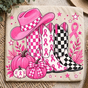 Puede incluir: Una camiseta beige con un estampado gráfico de un sombrero de vaquero rosa brillante, tres botas vaqueras con patrones de cuadros o cintas rosas y negras, y tres calabazas rosas. El diseño incluye estrellas, hojas y un lazo rosa.