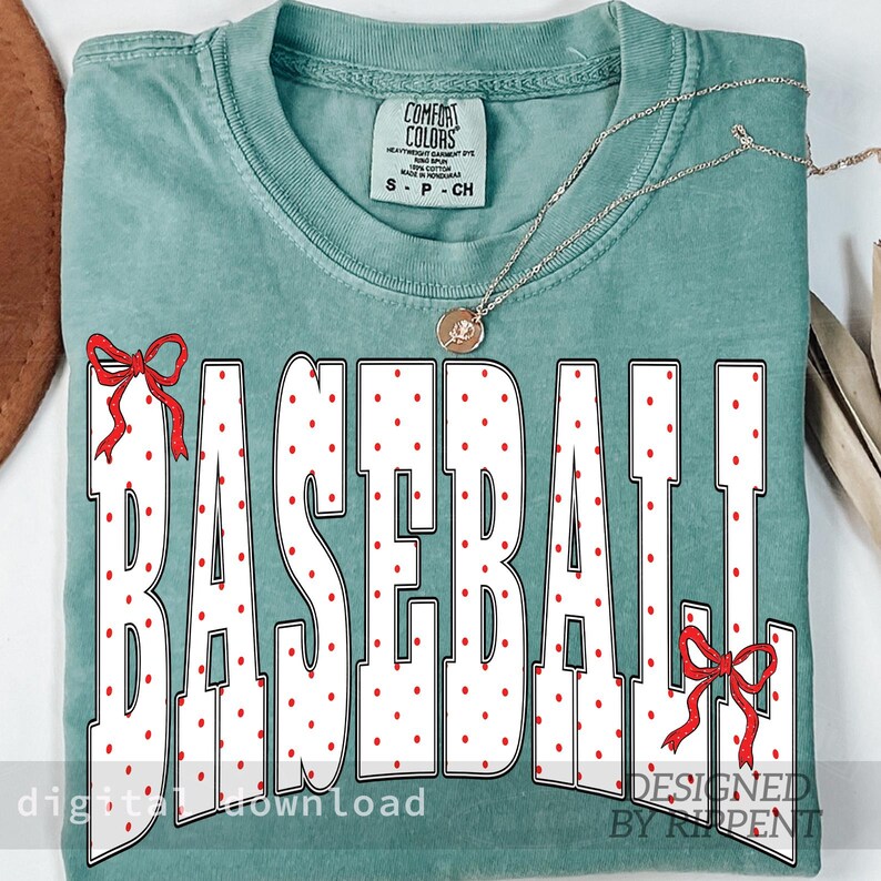May include: A teal-colored t-shirt with the word "BASEBALL" in large white letters with red polka dots. Red bows accent the top and bottom of the word. The shirt has a crew neck and short sleeves. The text "COMFORT COLORS" is printed on the upper part of the shirt.