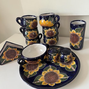 May include: A set of blue and yellow ceramic dishes with sunflower designs. The set includes a serving plate, four cups, a pitcher, and two salt and pepper shakers.