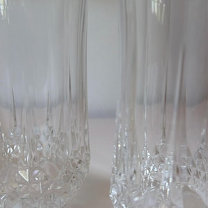 May include: Two clear glass tumblers featuring a vertical ribbed design on the upper portion and a textured diamond-cut pattern around the base. The glasses have a cylindrical shape with a slightly flared rim, showcasing a transparent finish.