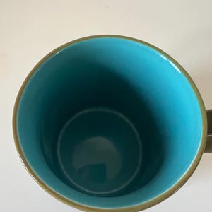 Puede incluir: Una taza de cer&aacute;mica con interior turquesa y borde y asa marrones. El interior de la taza es de un color turquesa vibrante, que contrasta con el borde y el asa marrones. La taza est&aacute; dise&ntilde;ada para bebidas fr&iacute;as o calientes.