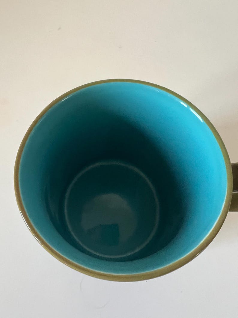 Puede incluir: Una taza de cer&aacute;mica con interior turquesa y borde y asa marrones. El interior de la taza es de un color turquesa vibrante, que contrasta con el borde y el asa marrones. La taza est&aacute; dise&ntilde;ada para bebidas fr&iacute;as o calientes.