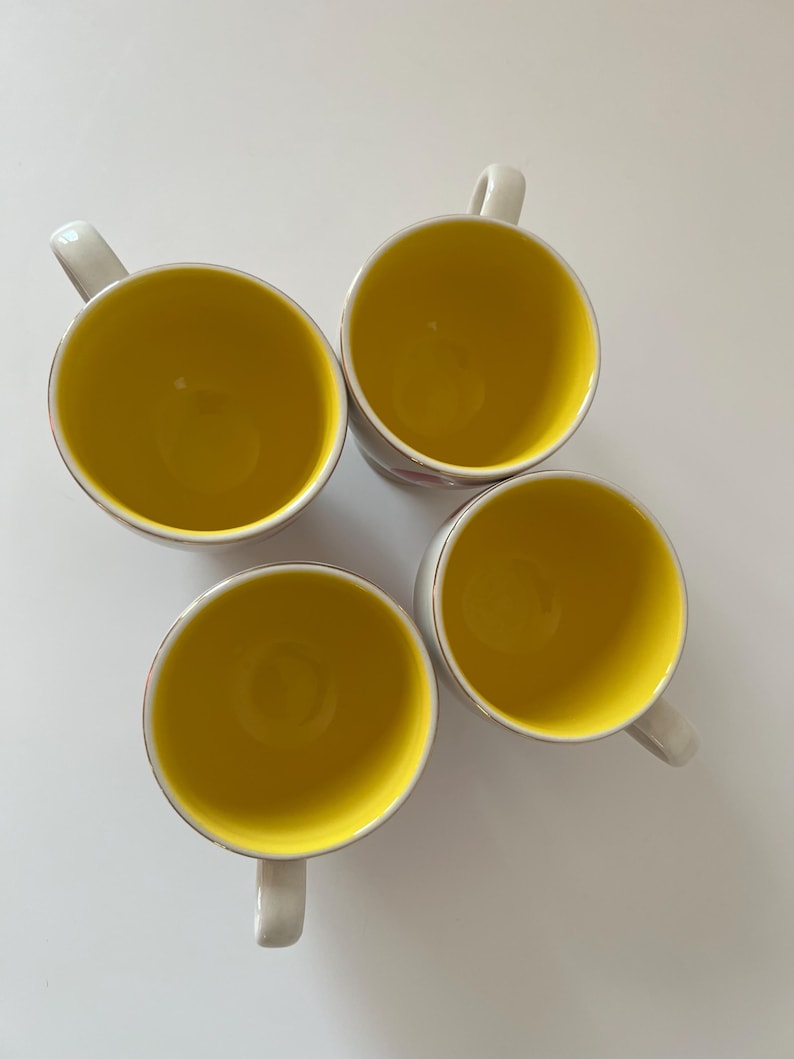 May include: Four white ceramic mugs with yellow interiors. The mugs have a simple design and are perfect for everyday use.