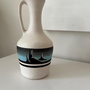May include: White ceramic pitcher with a black and blue painted design of a desert landscape with mountains and birds.