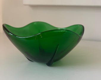 May include: A vibrant green glass bowl with a unique, wavy rim. The bowl has a smooth, glossy finish and rests on three small, curved feet. This decorative piece is ideal for displaying small items or as a standalone accent.