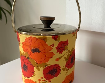 May include: A vintage ice bucket with a silver lid and a floral pattern. The bucket has a handle and a wooden knob on the lid. The floral pattern is red, orange, and yellow on a cream background.