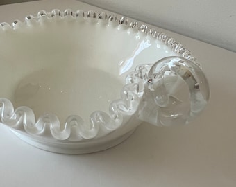 May include: White glass serving bowl with a scalloped edge and a clear glass handle. The bowl has a vintage look.