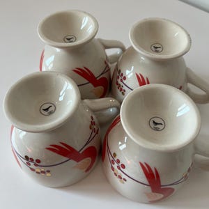 May include: Set of four white ceramic mugs with red and gold floral designs. Each mug has a small bird logo on the bottom.