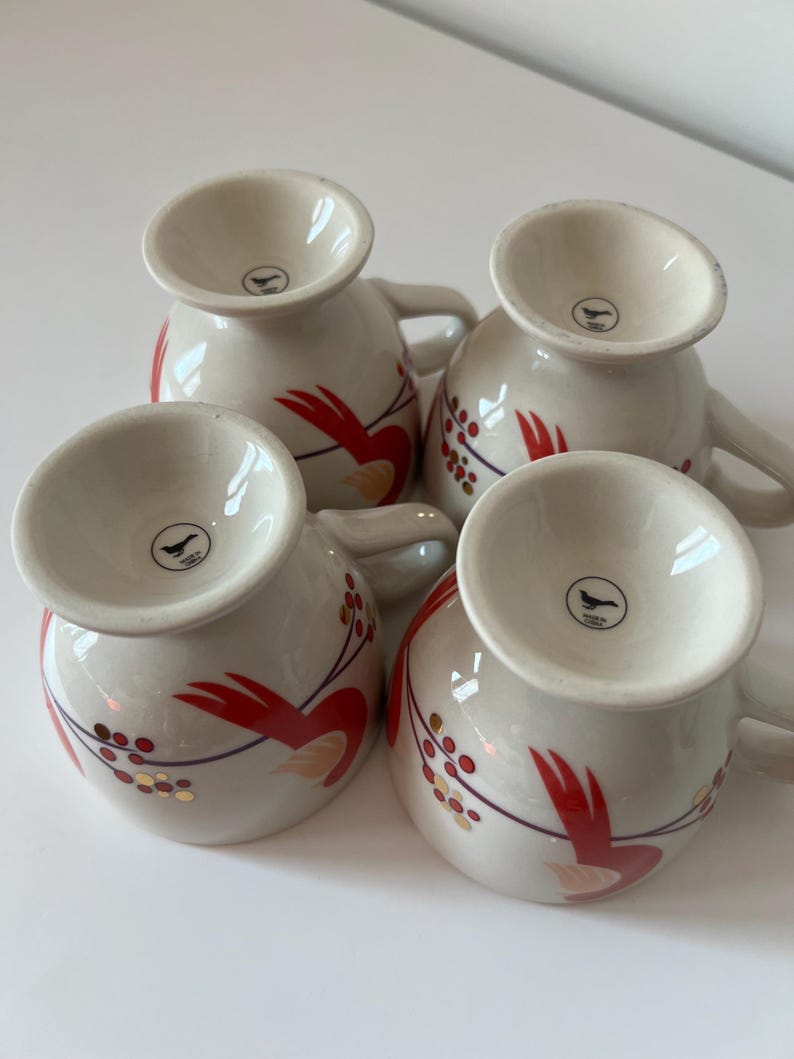 May include: Set of four white ceramic mugs with red and gold floral designs. Each mug has a small bird logo on the bottom.