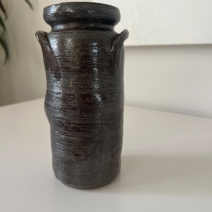 May include: A dark brown ceramic vase with two small handles on the sides. The vase has a textured surface and a slightly rounded shape.