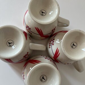 May include: Set of four white ceramic mugs with red and gold floral designs. Each mug has a black bird logo on the bottom.