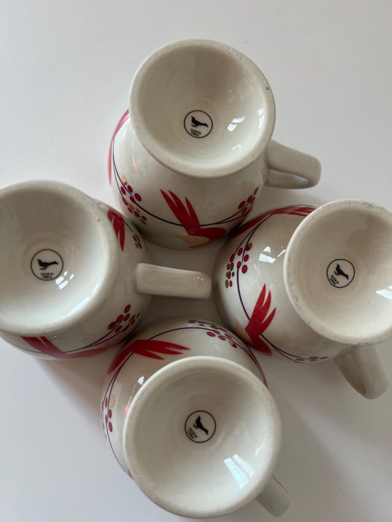 May include: Set of four white ceramic mugs with red and gold floral designs. Each mug has a black bird logo on the bottom.