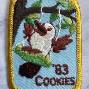 May include: A blue and brown embroidered patch with a bird on a swing. The text "83 Cookies" is below the bird.