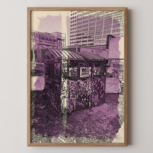 Può includere: Una stampa incorniciata con una scena urbana dai toni viola. L'opera raffigura una piccola struttura ricoperta di graffiti sullo sfondo di edifici. La stampa ha un'estetica vintage e artistica, con un focus sulle trame e sui dettagli.