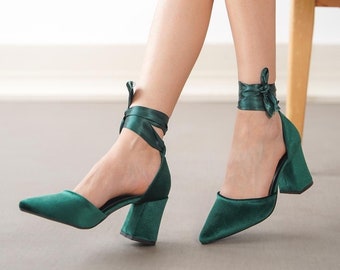 May include: A pair of dark green velvet heels with a pointed toe and a block heel. The heels have a satin ribbon that ties around the ankle.
